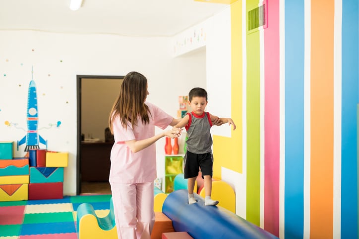 pediatric therapist helping small child walk across padded balance beam
