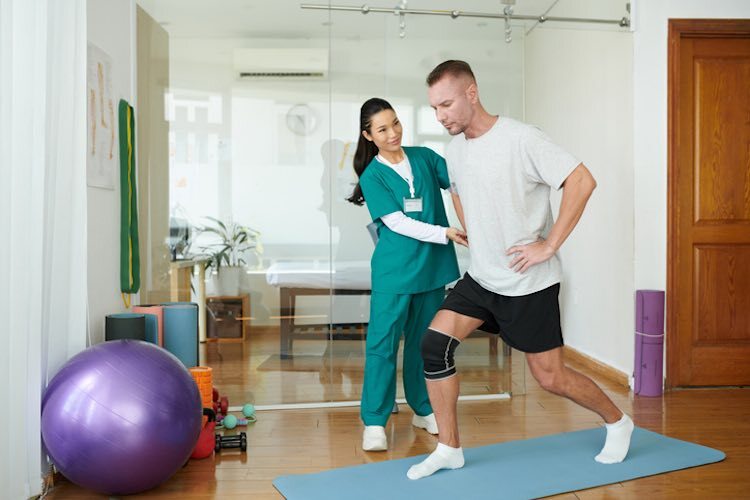 Physical therapist guiding patient through knee rehabilitation exercise using balance mat