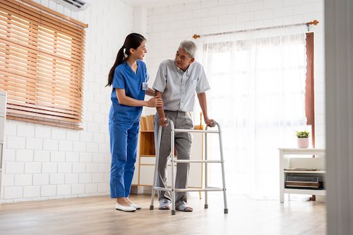 Physical therapist supporting elderly man with walker during mobility training
